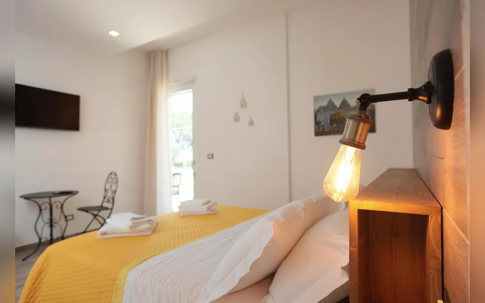 Il letto con la lampada a muro e la TV a parete